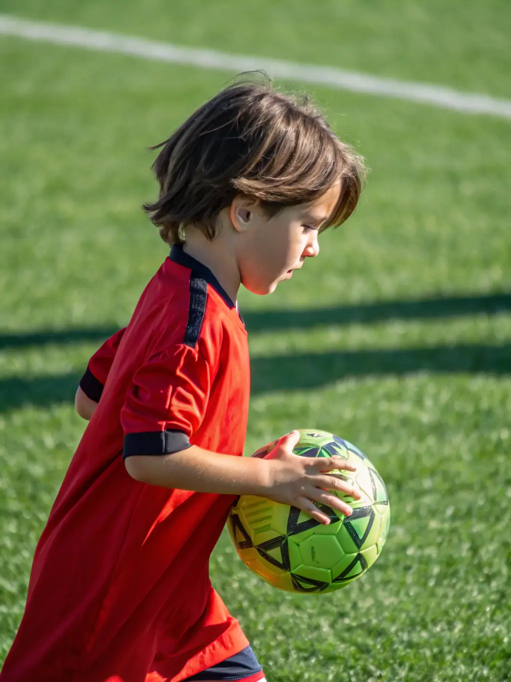 A young football player dribbling a ball with determination, emphasizing the health benefits of regular physical activity.